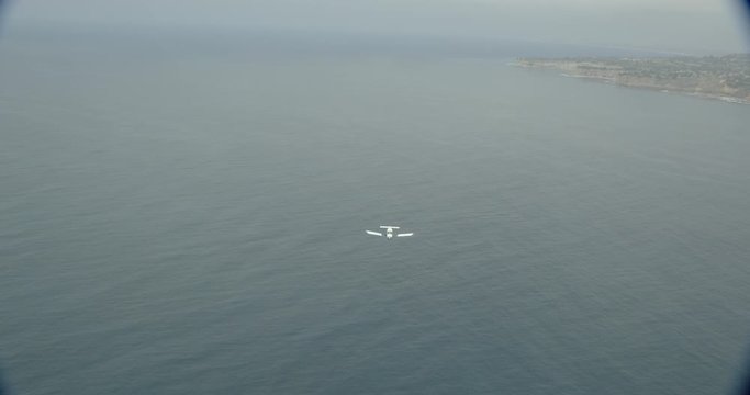Helicopter aerial shot far ahead of small jet plane flying over ocean, foggy day