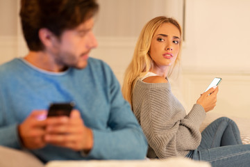 Husband Texting On Cellphone Sitting With Suspicious Wife At Home