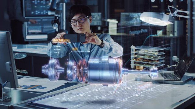 Industrial Engineer Works with Smartphone Using Augmented Reality Holographic Projection 3D Model of the Enlectric Motor Prototype. Development of Virtual Mixed Reality Application.