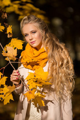 Portrait of pretty blonde teen girl with fashion makeup near autumn tree with yellow leaves