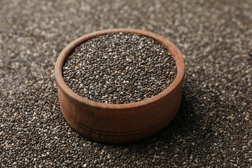 Wooden bowl and chia seeds on whole background, space for text