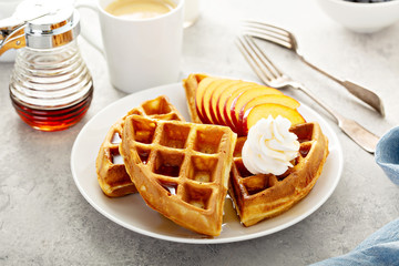 Peach waffles for breakfast served with fresh berries, maple syrup and coffee