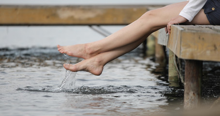A woman sits on a pier and splashes water. Close-up of bare female legs on a lake.