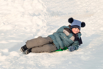 Fototapeta na wymiar Child slid down a snow slide and is happy lies on an ice-boat. Sledding from a snow plate.