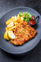 Deep fried Wiener schnitzel from veal topside with French fries and lettuce as closeup on a modern design plate