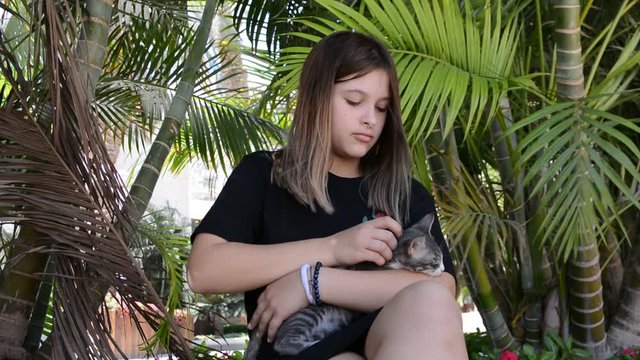 Cat laying in the arms of teengirl. Teengirl in black shirt standing by a street holding a cat snuggled in her arms like a baby.