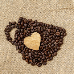 Coffee beans in the shape of a coffee cup with carved wooden heart on natural canvas, sackcloth. Concept of coffee love, loved one