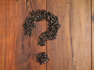Question mark made from sunflower seeds on a brown wooden table surface. Top view.