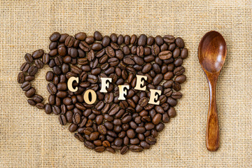 Roasted coffee beans in the shape of cup close-up with word coffee and wooden spoon on natural canvas, sackcloth
