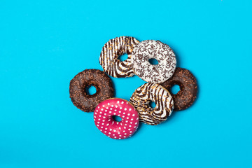Colorful donuts with icing on blue background. Donuts forming a circle, Top view with copy space, realistic style.