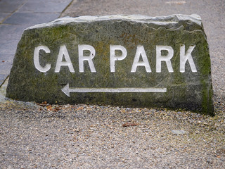Car park sign on a stone with an arrow pointing to the left.
