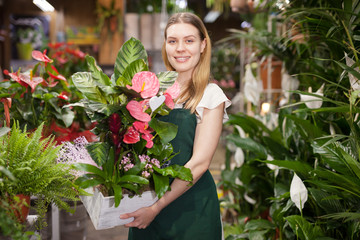 Сheerful woman florist holding pot with a flower in the gardening market
