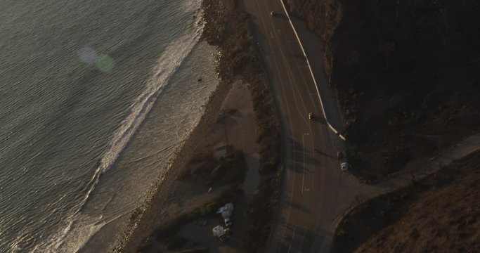 Helicopter aerial birds eye view shot moving down where shore meets PCH highway, sundown