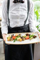 The waiter is holding a plate Grilled vegetables with feta cheese. Serving on a plate on a table. Barbecue restaurant menu, a series of photos of different dishes