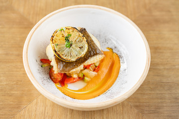 Roasted pike perch or cod fish with baked vegetables. Dish decorated with a slice of lemon. Restaurant menu