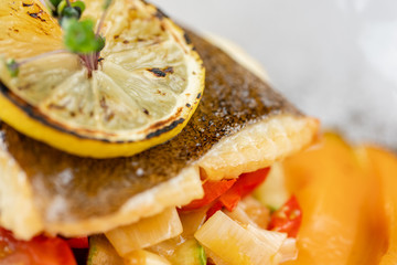 Roasted pike perch or cod fish with baked vegetables. Dish decorated with a slice of lemon....
