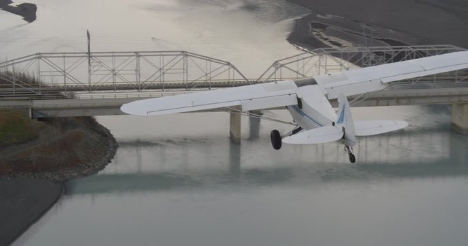 Helicopter aerial shot of biplane flying over bridge then descending over dry river, drone