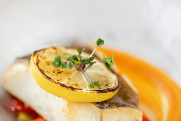 Roasted pike perch or cod fish with baked vegetables. Dish decorated with a slice of lemon. Restaurant menu