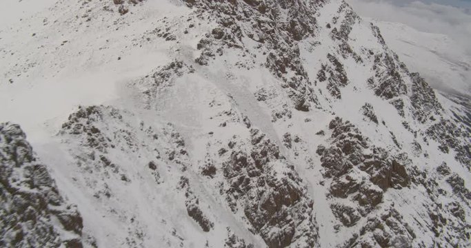 Aerial helicopter shot, twist around snowy, rocky mountainside to reveal peak, drone footage