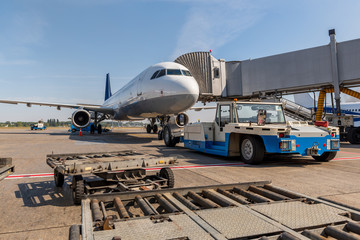Pushback car is ready to tow a passenger plane, which stands near the telescope gate. Airport life and travel concept
