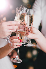 Four friends clink glasses of champagne with lights behind.