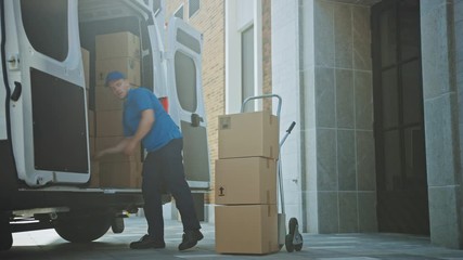 Delivery Man Uses Hand Truck Trolley Full of Cardboard Boxes and Packages, Loads Parcels into Truck / Van. Professional Courier / Loader helping you Move, Delivering Your Purchased Items Efficiently