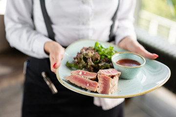 The waiter is holding a plate medium rare tuna with lettuce and hot sauce. Restaurant menu