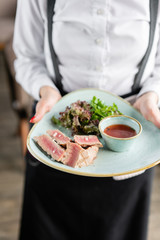 The waiter is holding a plate medium rare tuna with lettuce and hot sauce. Restaurant menu