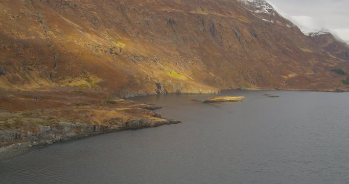 Aerial helicopter shot, past orange hillside with numerous small waterfalls feeding into large Alaskan lake, drone footage