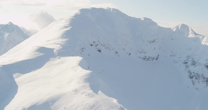 Aerial helicopter shot, push in on snowy mountain peak, reveals sprawling snowy mountain, drone footage