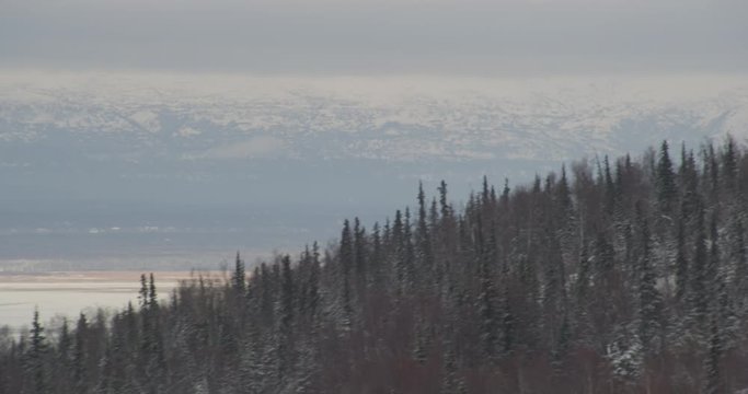  Aerial helicopter wide shot over winter forest, push past cabins and up hill into fog bank, drone footage