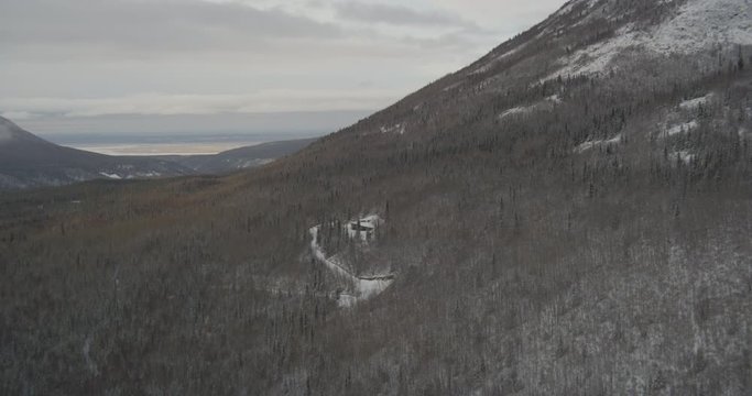  Aerial helicopter wide shot, over mountainside home in the snowy trees, drone footage