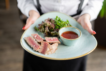 The waiter is holding a plate medium rare tuna with lettuce and hot sauce. Restaurant menu