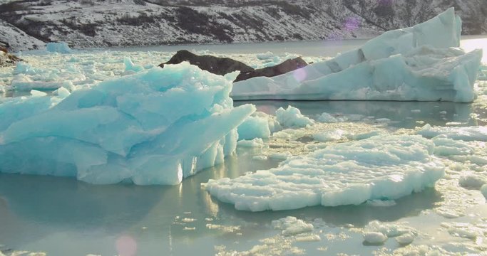  Aerial helicopter shot, closeup details over splintered ice floes and icebergs in mountain lake at golden hour, drone footage