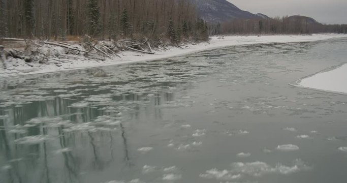  Aerial helicopter fly low over icy river, ice floes on water, mountains in distance, drone footage