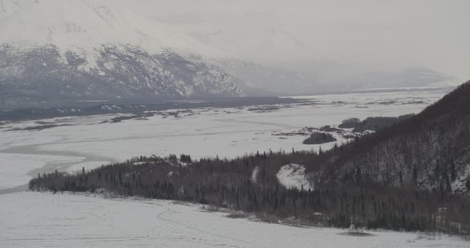  Aerial helicopter wide shot, across peninsula near frozen river in snowy mountain valley, drone footage