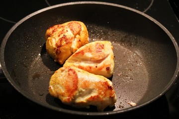 Three pieces of chicken breast meat fried in a large pan