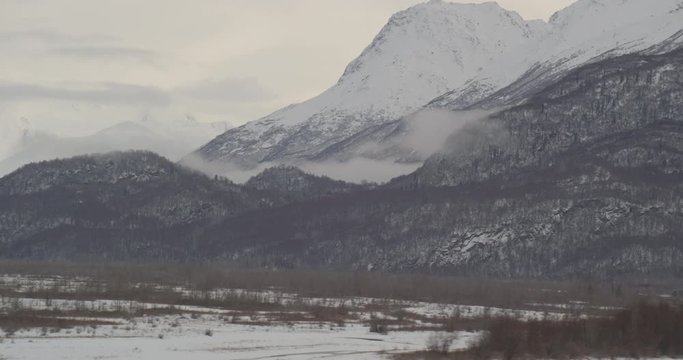  Aerial helicopter shot, track across frozen river with foggy, snowy mountainsides in the distance, drone footage