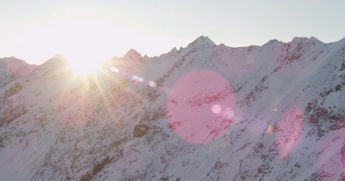 Aerial helicopter shot, tracking across a rocky, snowy Alaskan mountain range cast in shadow during golden hour, drone footage, lens flare