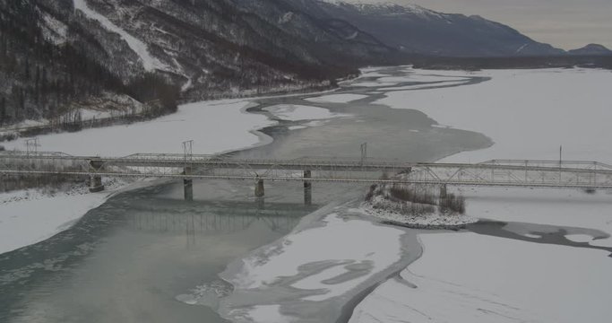  Aerial overhead helicopter shot, circle around track man as he stands in the center of a snowy Alaskan bridge, he listens to a walkie talkie before walking off, drone footage