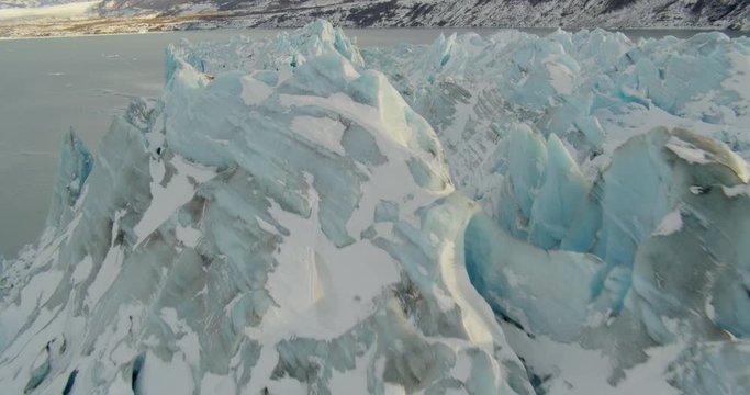  Aerial helicopter closeup details tracking overhead glacial ice in mountain lake at golden hour, tilt down to water, drone footage