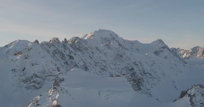  Aerial helicopter shot, tracking across a rocky, snowy mountain at golden hour, tilt down over mountain peak, drone footage