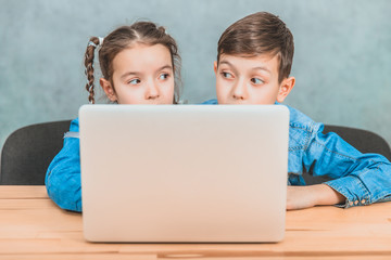 Cute little schoolkids sitting at the desk, puzzled by something they have seen in the laptop.