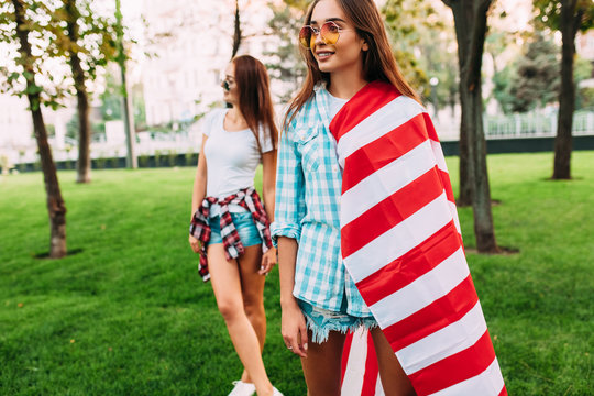 Two stylish attractive girls with an American flag, posing in the Park in the summer