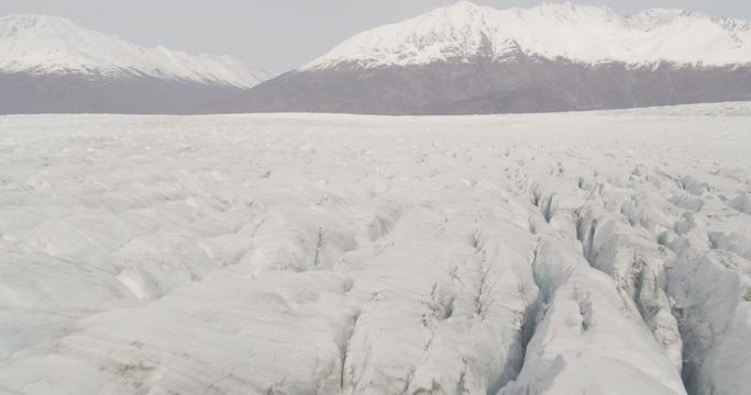 Aerial shot, day, medium altitude fly over glacier in valley, mountains in distance, drone