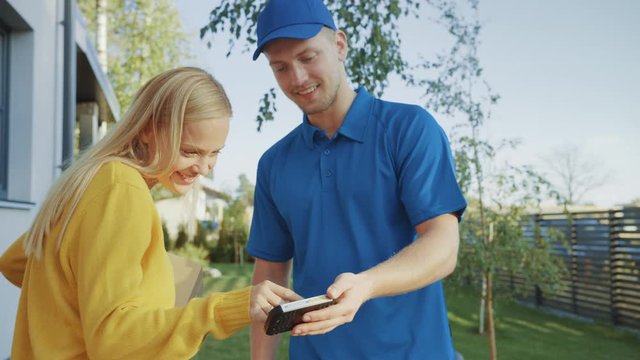 Beautiful Young Woman Meets Delivery Man who Gives Her Cardboard Box Package, She Signs Electronic Signature POD Device. Courier Delivering Parcel in the Suburban Neighborhood. Side View 