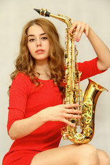 Obraz premium A beautiful girl in a red dress sits and holds in her hands a golden saxophone