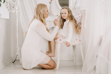 Beautiful woman and child girl doing make up each other on white room background