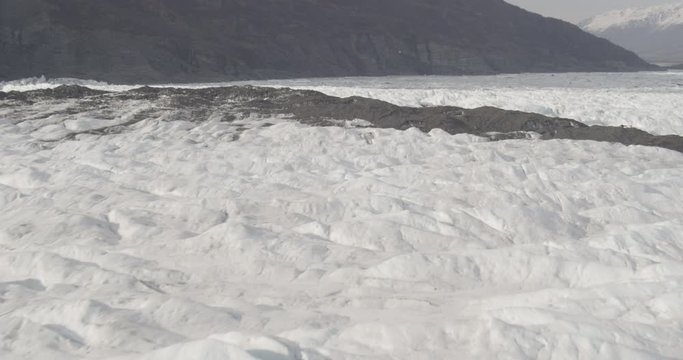 Aerial shot, day, fly over jagged glacier, mountain foothills in distance, drone