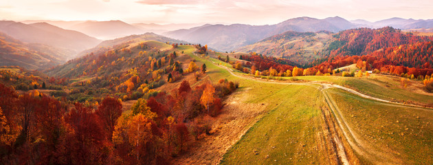 Autumn mountain panorama. Dirt road on top of the hills.